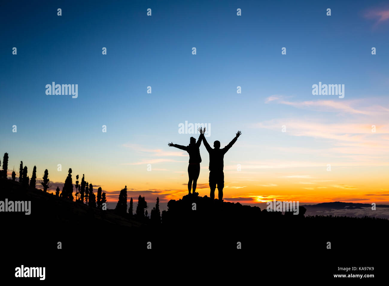 Teamwork couple climbing and reaching mountain peak. Silhouette of climbers team over mountains sunset. Man and woman hikers looking at inspirational  Stock Photo