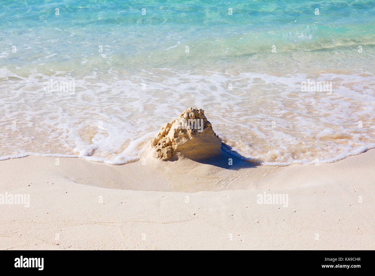 Sandcastle on the beach being washed away by the waves - concept of ...