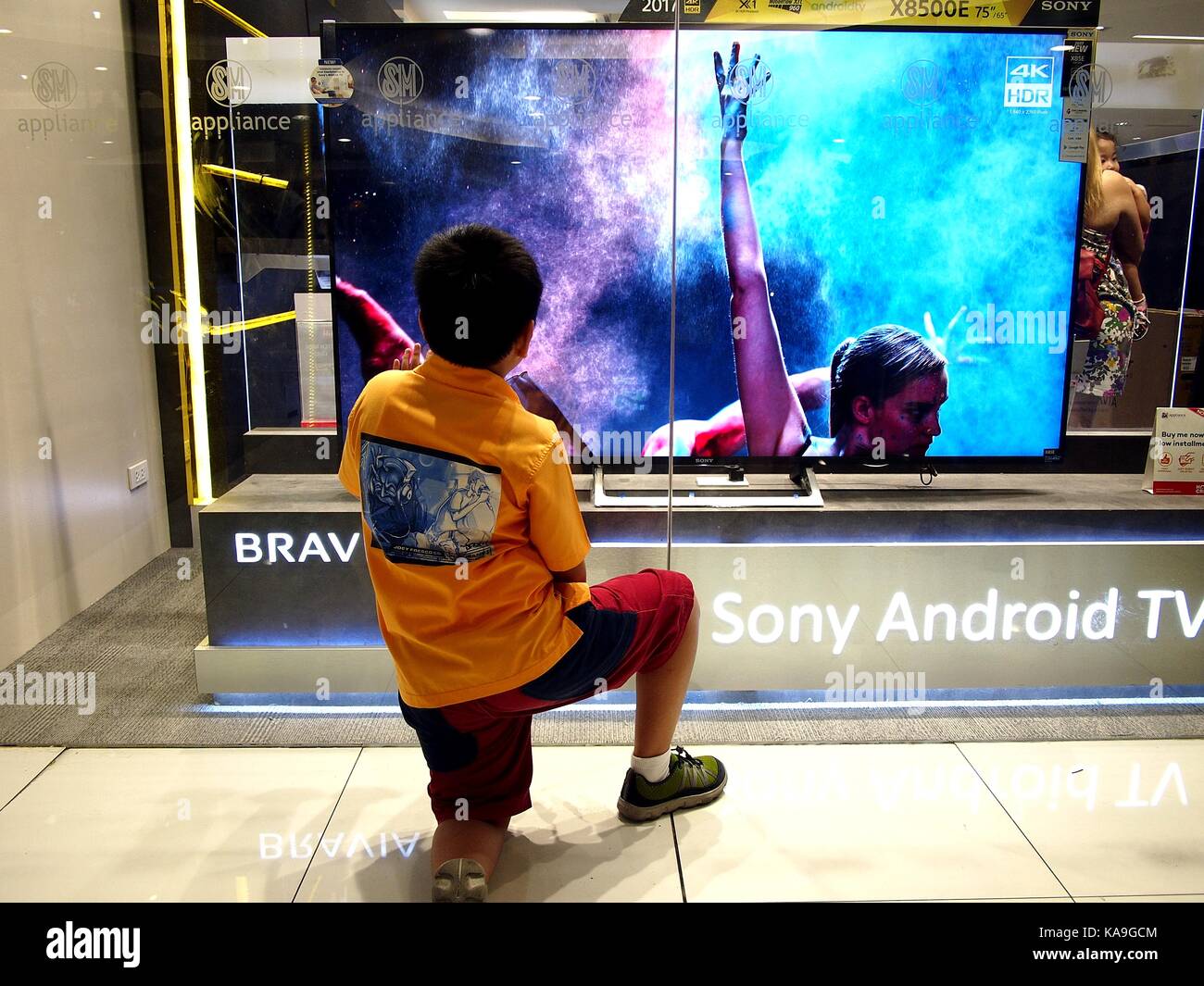 MANDALUYONG CITY, PHILIPPINES - SEPTEMBER 24, 2017: A young boy watches TV outside an electronics shop. Stock Photo