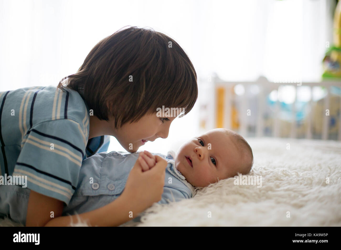 Beautiful boy, hugging with tenderness and care his newborn baby brother at home. Family love happiness concept Stock Photo