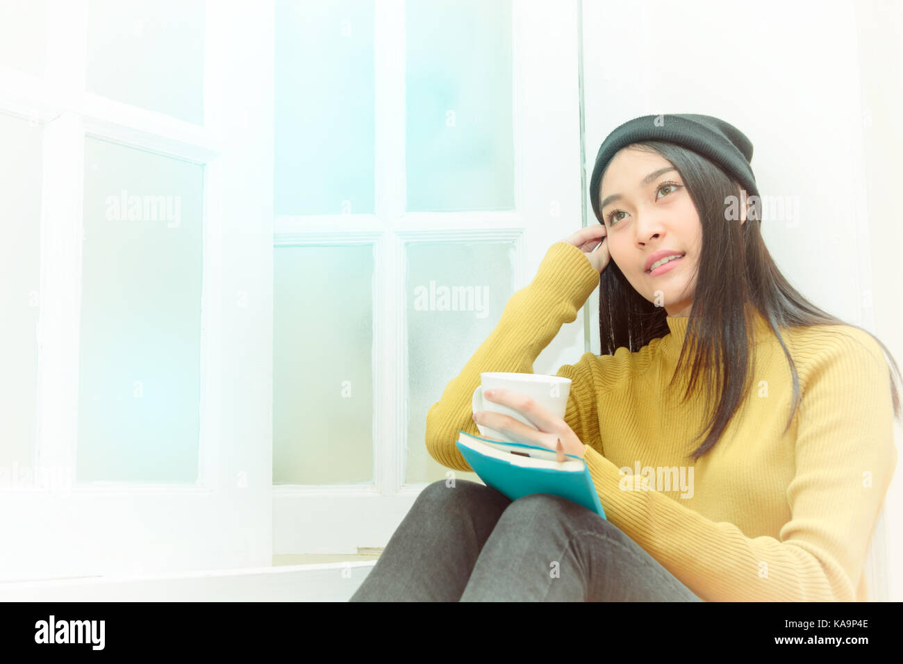 Beautiful Asian woman sitting near the window and holding a cup of ...
