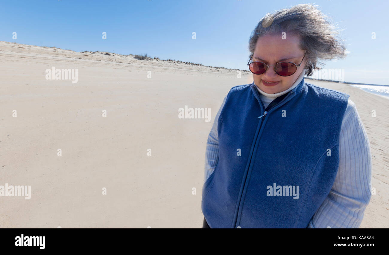 A senior woman walks alone on a beach contemplating life. Stock Photo