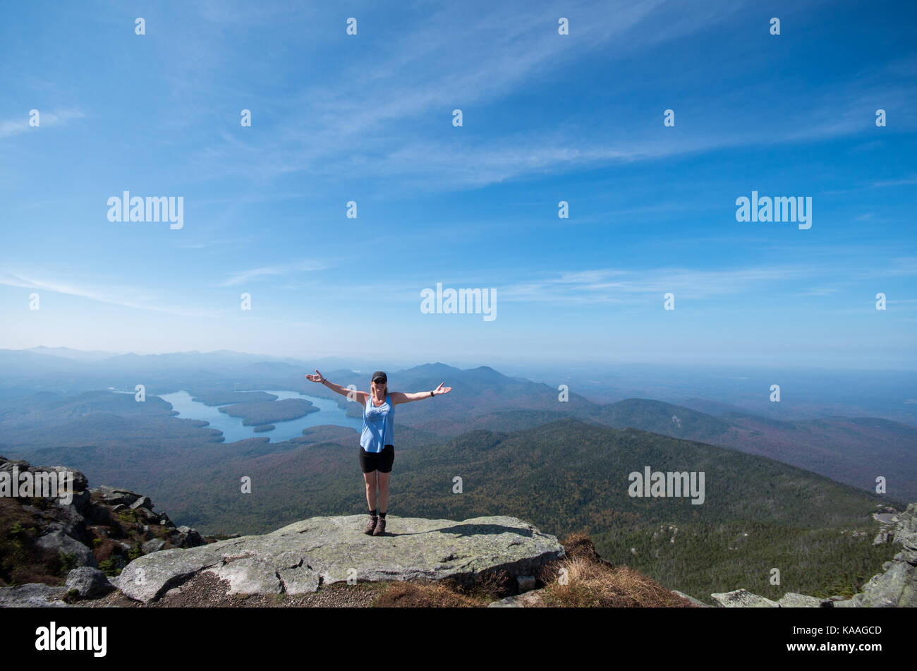 Female hiker standing on the edge of a cliff with her arms out at the summit of Whiteface Mountain Stock Photo