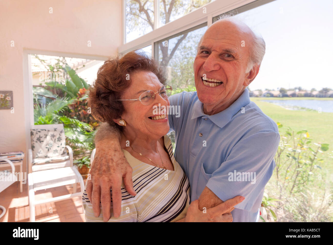 Wife with mild cognitive impairment (87 years-old) & husband (90 years-old), married 65 years, being affectionate & laughing, at home. Stock Photo