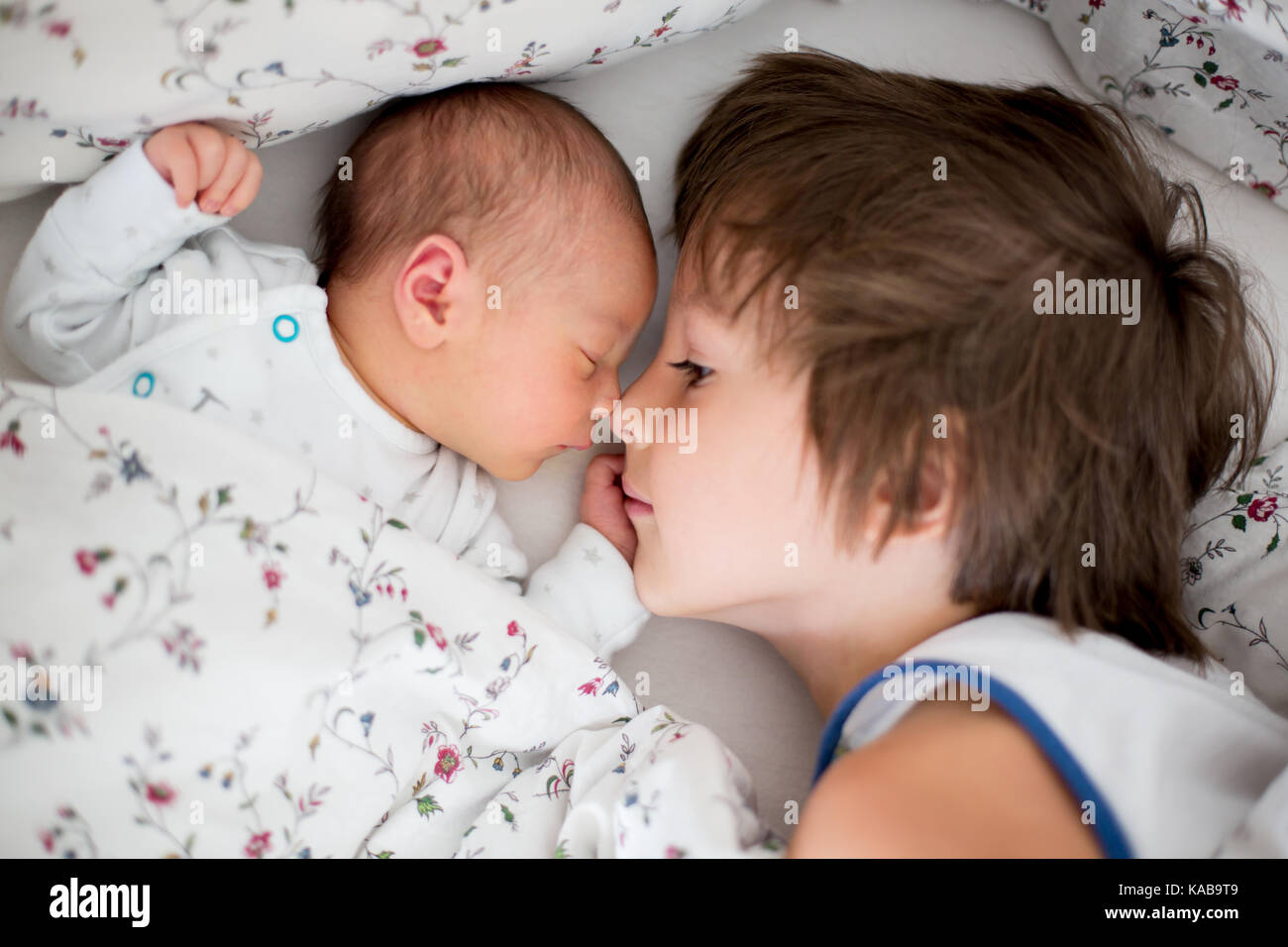 Beautiful boy, hugging with tenderness and care his newborn baby brother at home. Family love happiness concept Stock Photo