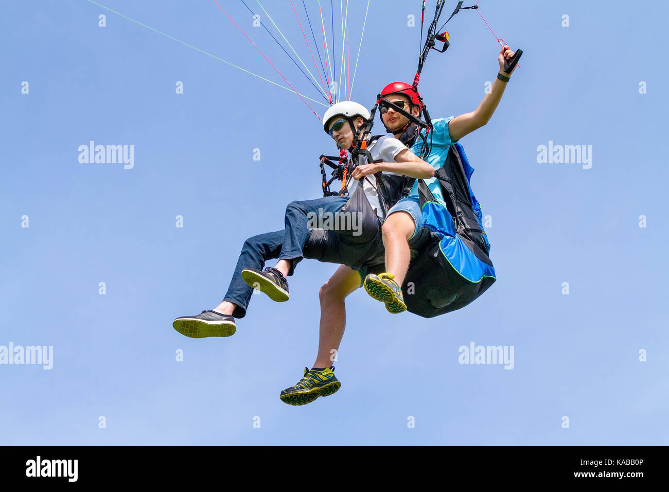 Instructor and paraglider boy floating in blue sky Stock Photo