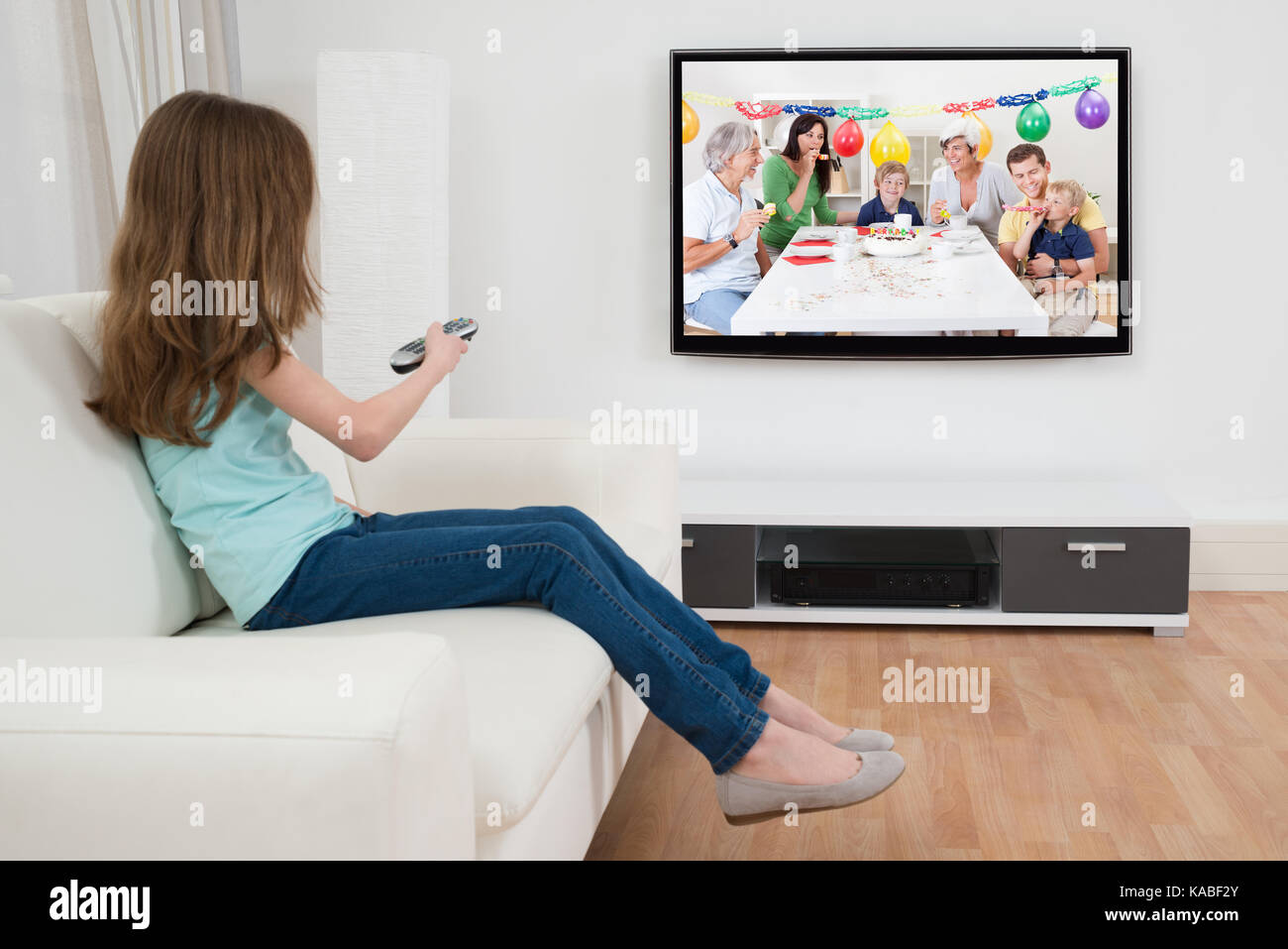 Girl Changing Channel With Remote Control In Front Of Television At Home Stock Photo