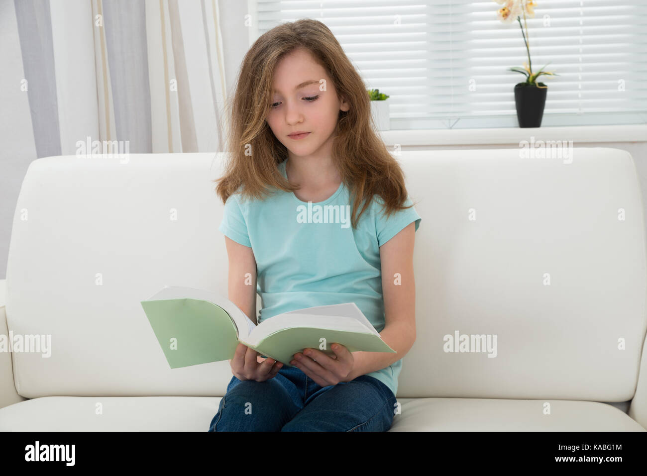 Girl Reading Book On Sofa In Living Room At Home Stock Photo - Alamy