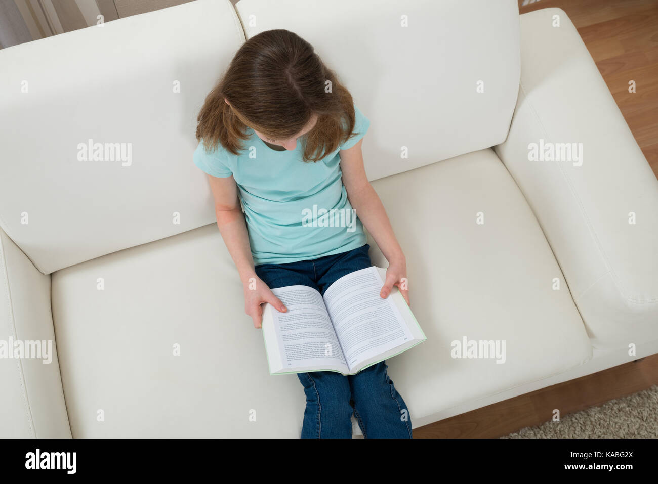 Girl Sitting On Sofa Reading Book In Living Room Stock Photo - Alamy