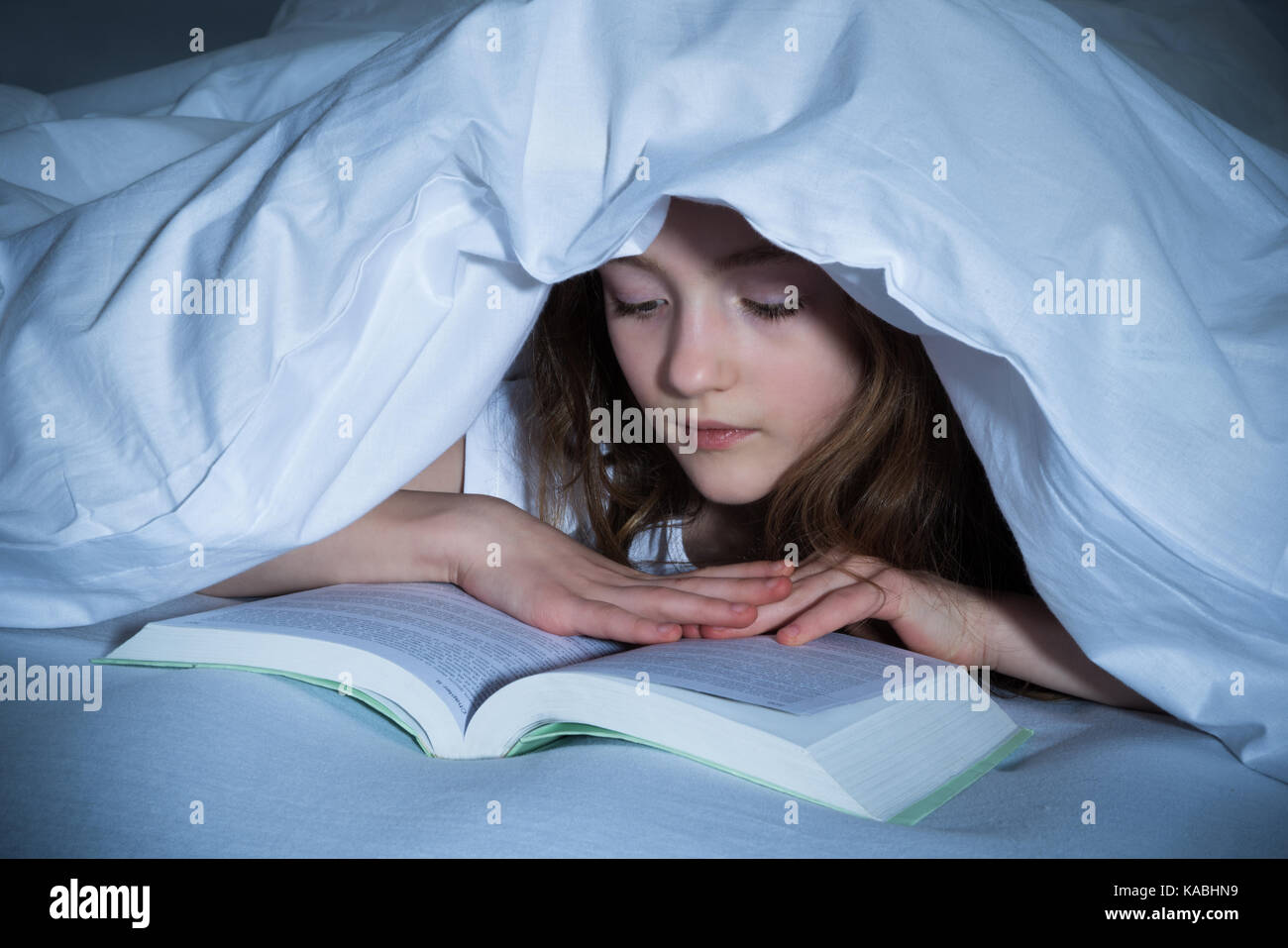 Cute Girl Reading Book Under The Blanket In Bedroom Stock Photo