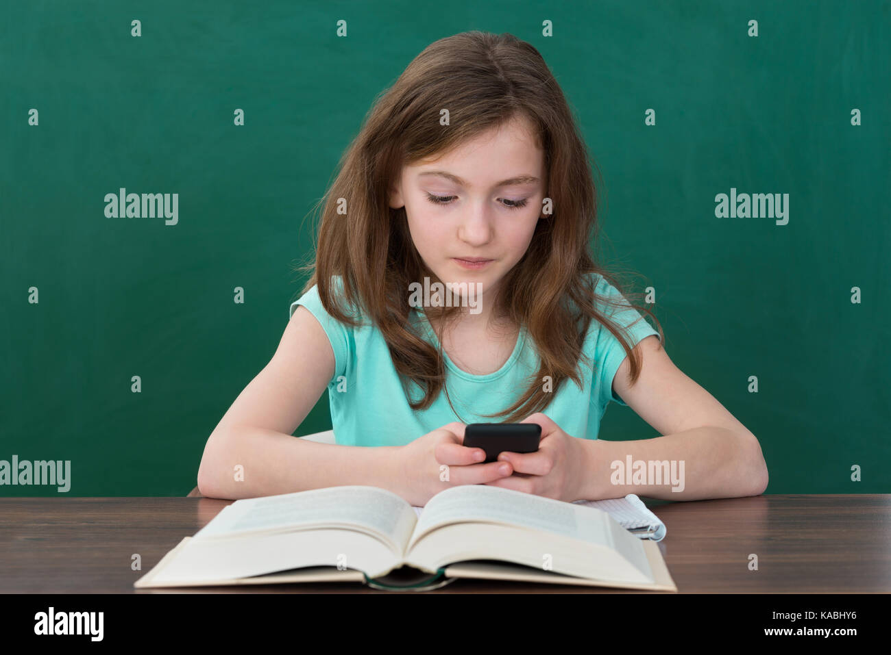 Girl Using Mobile Phone While Studying In Classroom Stock Photo