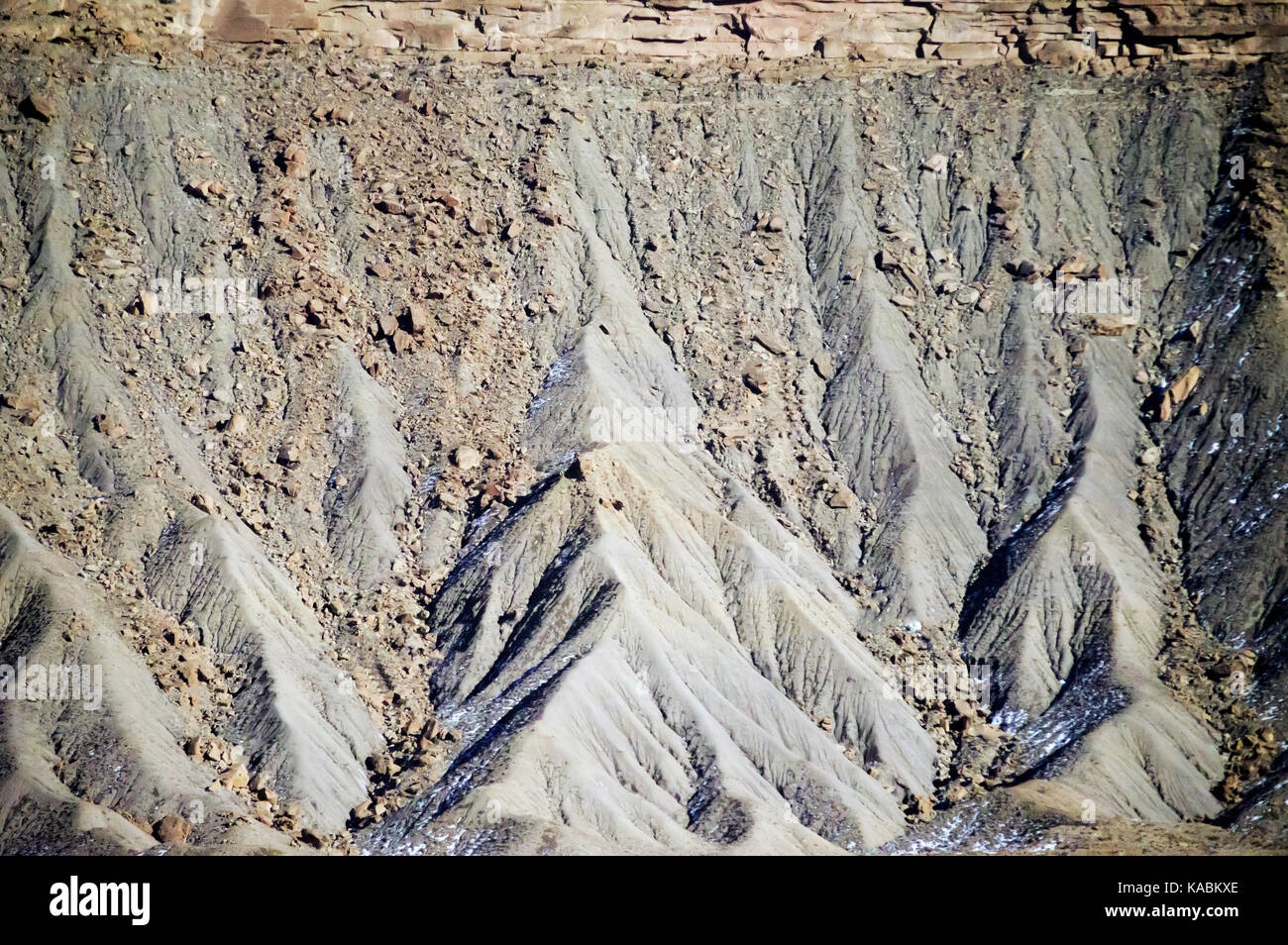 The side of rocky mountain on a bright blue sky with channels carved into it. Stock Photo
