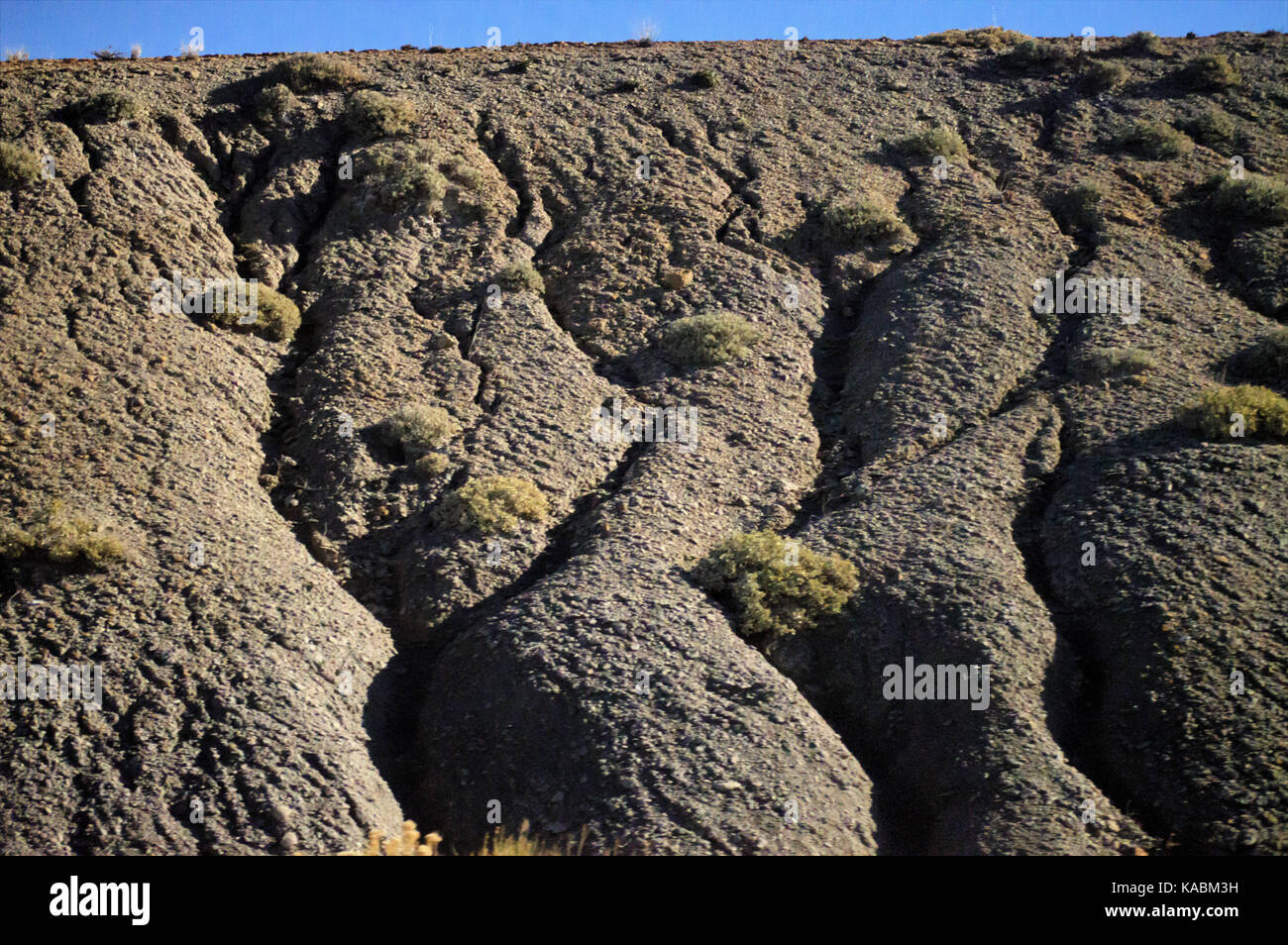 The side of rocky mountain on a bright blue sky with channels carved into it. Stock Photo