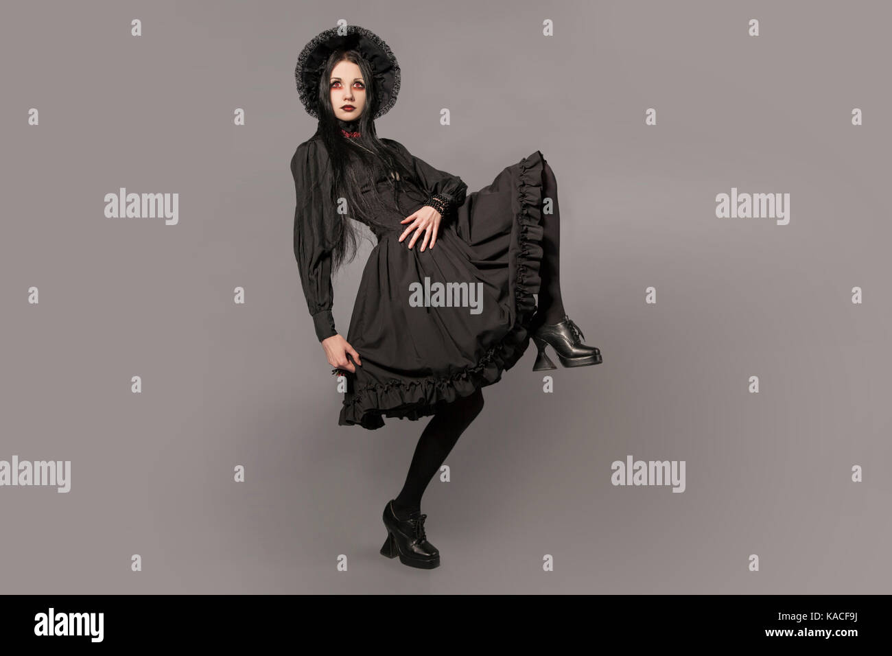 Portrait of brunette woman in black dress and classic gothic style with red eyes on gray background. halloween concept. Stock Photo