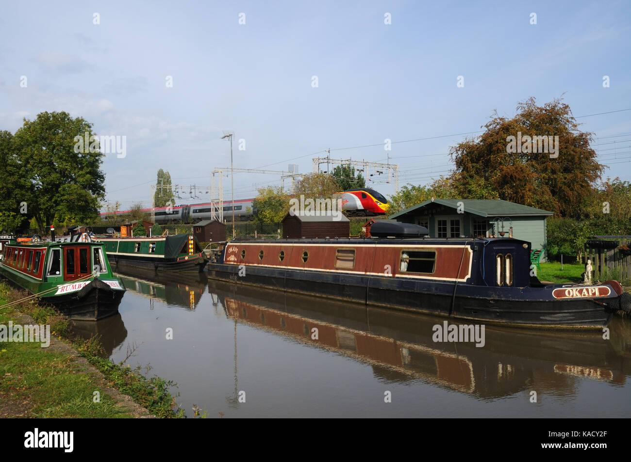 A Virgin Pendolino on the West Coast Main Line speeds past narrowboats moored on the Oxford Canal near Stretton-under-Fosse, Warwickshire, England Stock Photo