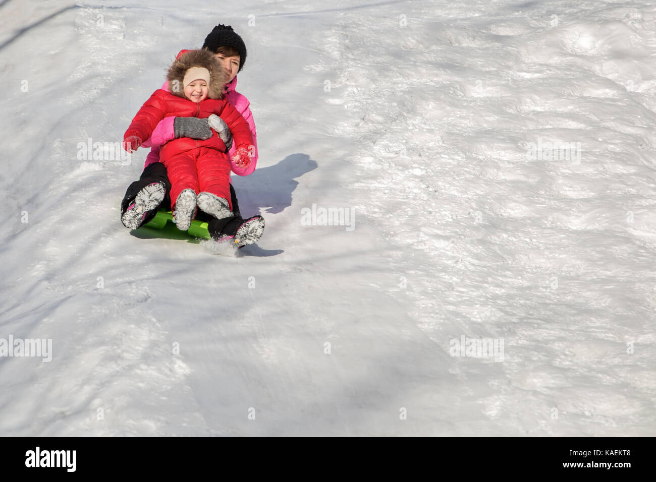 Happy mother and her daughter enjoying a sledge ride down the hills, winter games and fun. Family holiday and togetherness. Stock Photo