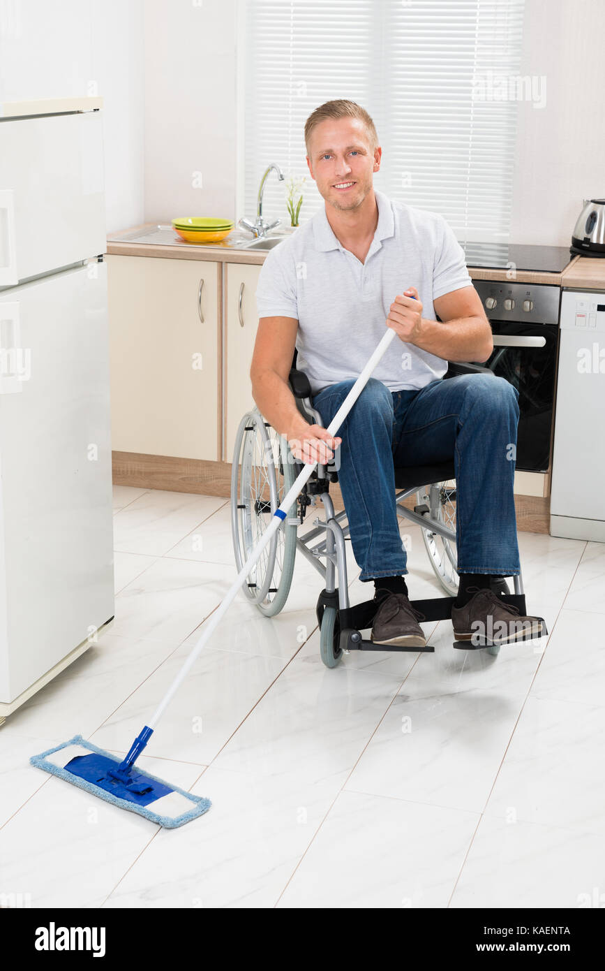 Disabled Man On Wheelchair Cleaning Floor With Mop In Kitchen Room