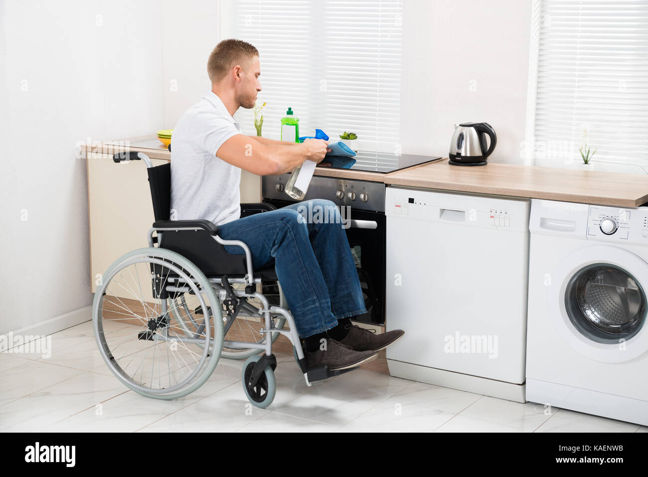 Young Handicapped Man On Wheelchair Cleaning Induction Stove Stock