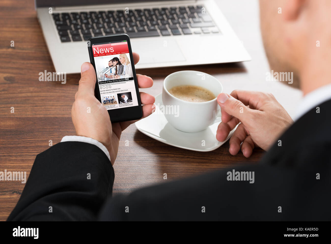 Close-up Of A Businessman Reading News On Cellphone While Having Coffee Stock Photo