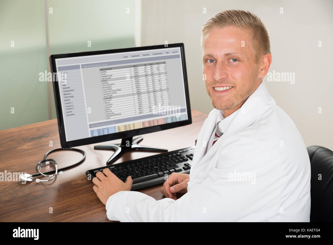 Young Happy Male Doctor Working On Computer At Desk Stock Photo