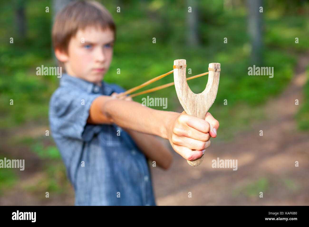Boy aiming wooden slingshot outdoors, , focus on a slingshot face is blurred Stock Photo