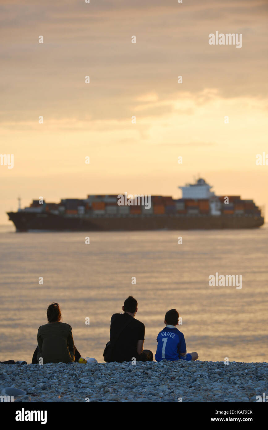 Le Havre (Normandy region, north western France): family on the pebble beach and container ship off the coast sailing back to the port Stock Photo