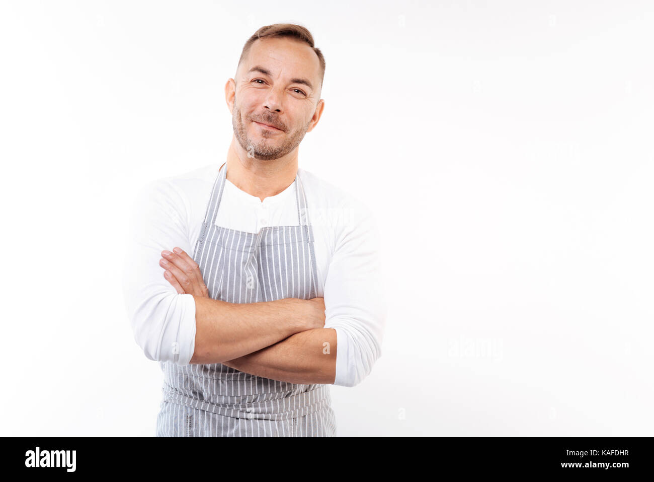 Smiling man in apron folding his arms across chest Stock Photo