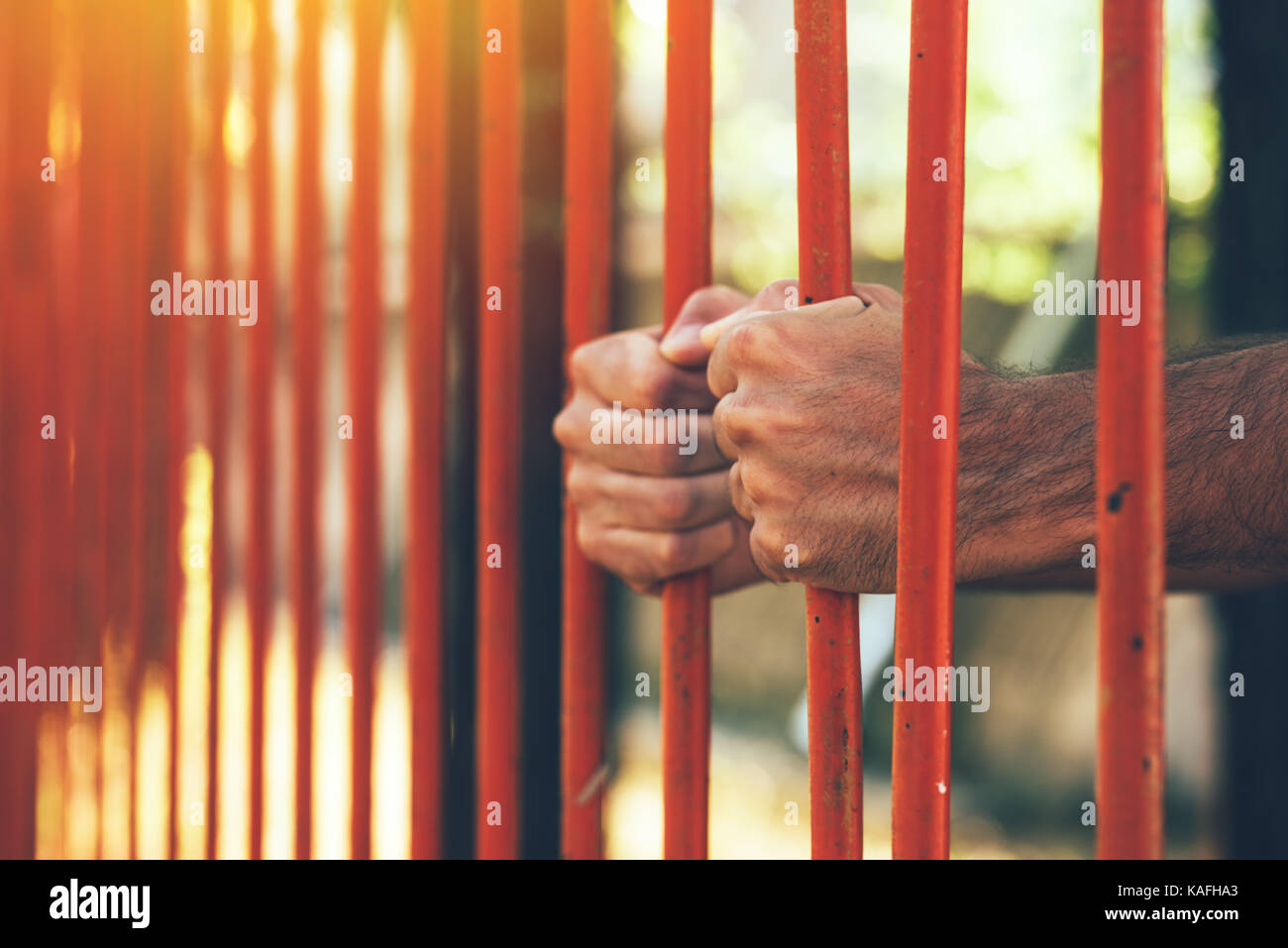 Male hands behind prison yard bars, incarcerated captivated person in jail Stock Photo