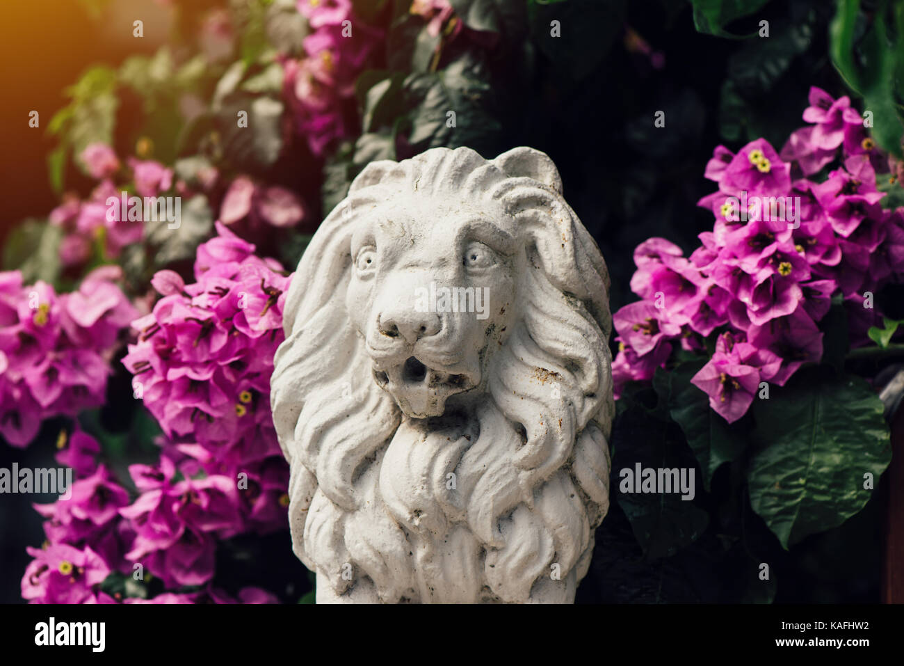 Small concrete sculpture of lion among flowers, home front yard decoration element Stock Photo