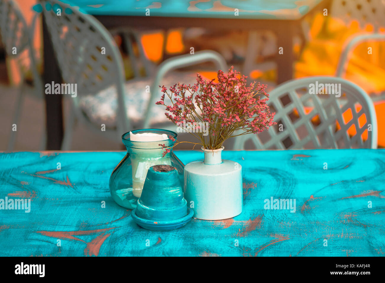 Modern hipster style teal and orange table arrangement in cafe or restaurant - flowers in pot, ashtray and candle Stock Photo