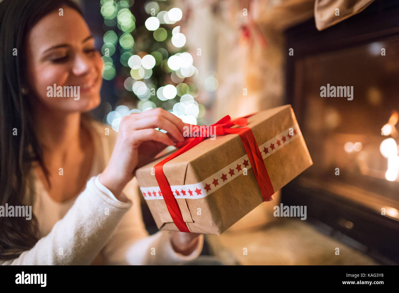 Woman in front of Christmas tree holding present Stock Photo - Alamy