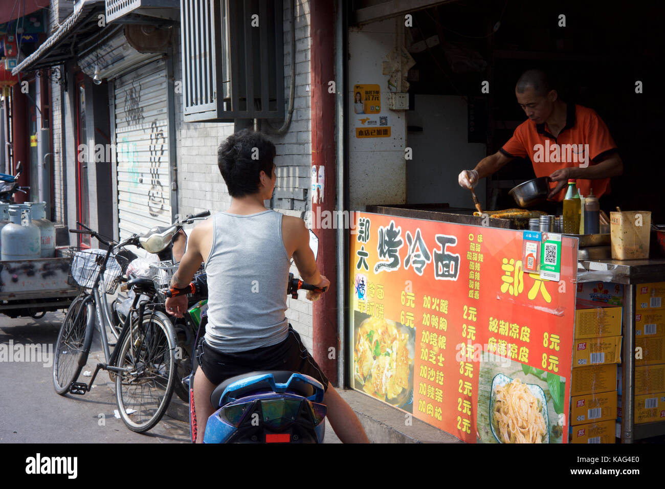 BEIJING, CHINA - SEP 21, 2017 : A man on his electric scooter is buying Chinese snacks from a local food stall at Andingmen Stock Photo