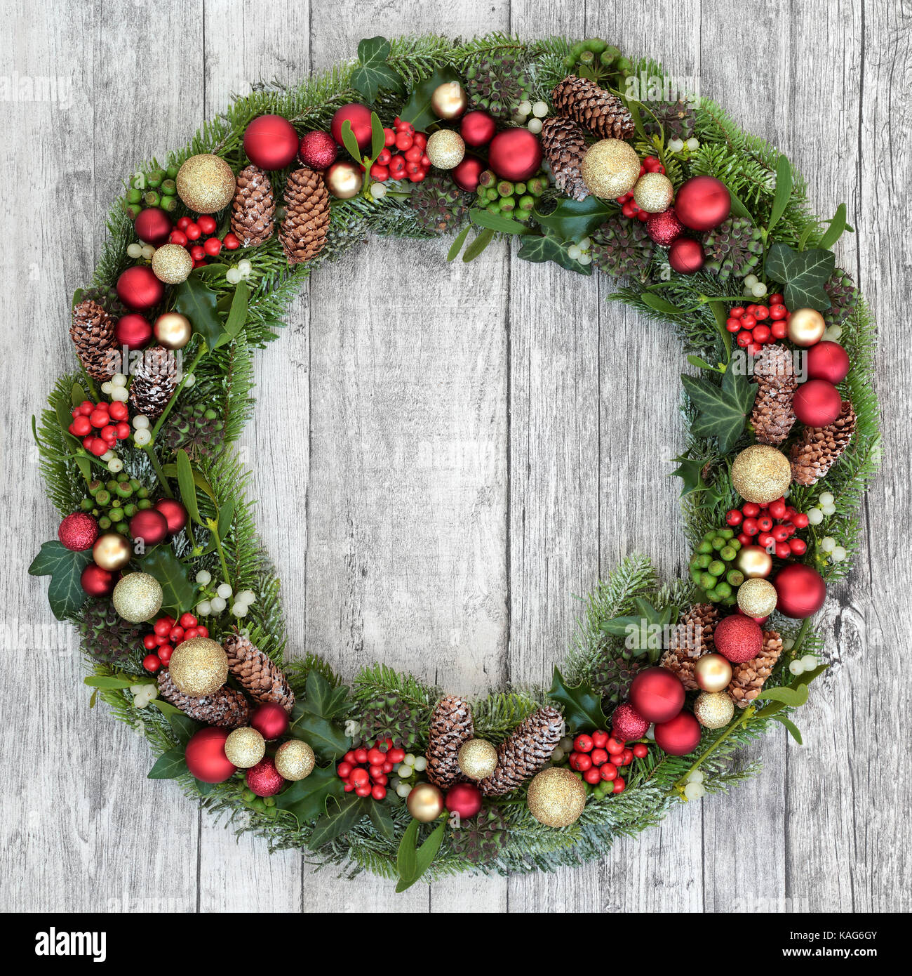 Christmas wreath decoration with baubles, holly, mistletoe, snow covered fir, blue spruce, ivy and pine cones on rustic white wood background. Stock Photo