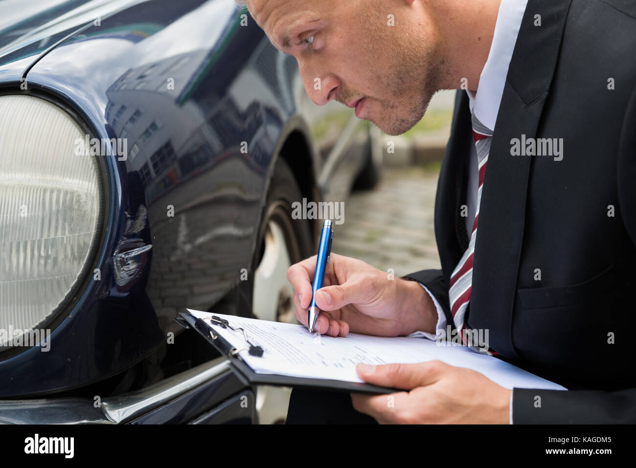 Close-up Of A Man Filling Insurance Form Near Damaged Car Stock Photo