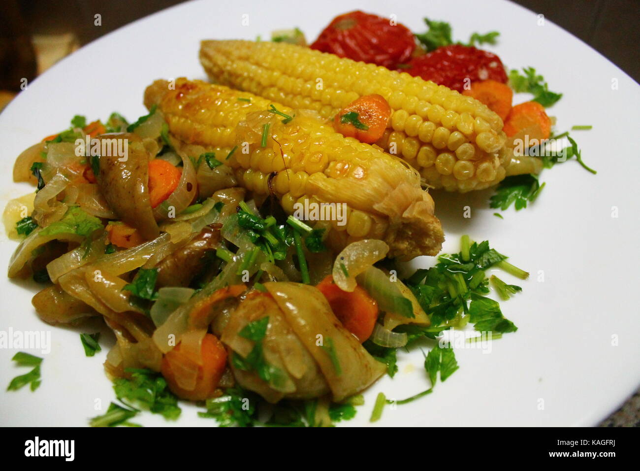 appetizing rolls of yellow sweet corn with tomato and pepper lay on white plate prepare for meal Stock Photo