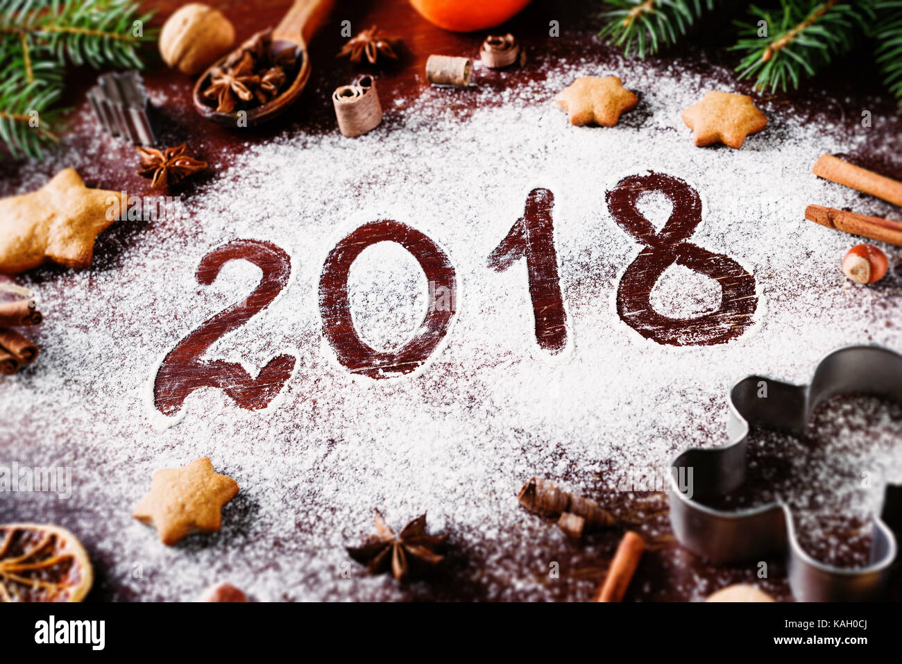 Happy New Year 2018 written on flour and Christmas Decorations Gingerbread cookies, cinnamin, oranges, spices, nuts and cookie cutters on wooden backg Stock Photo