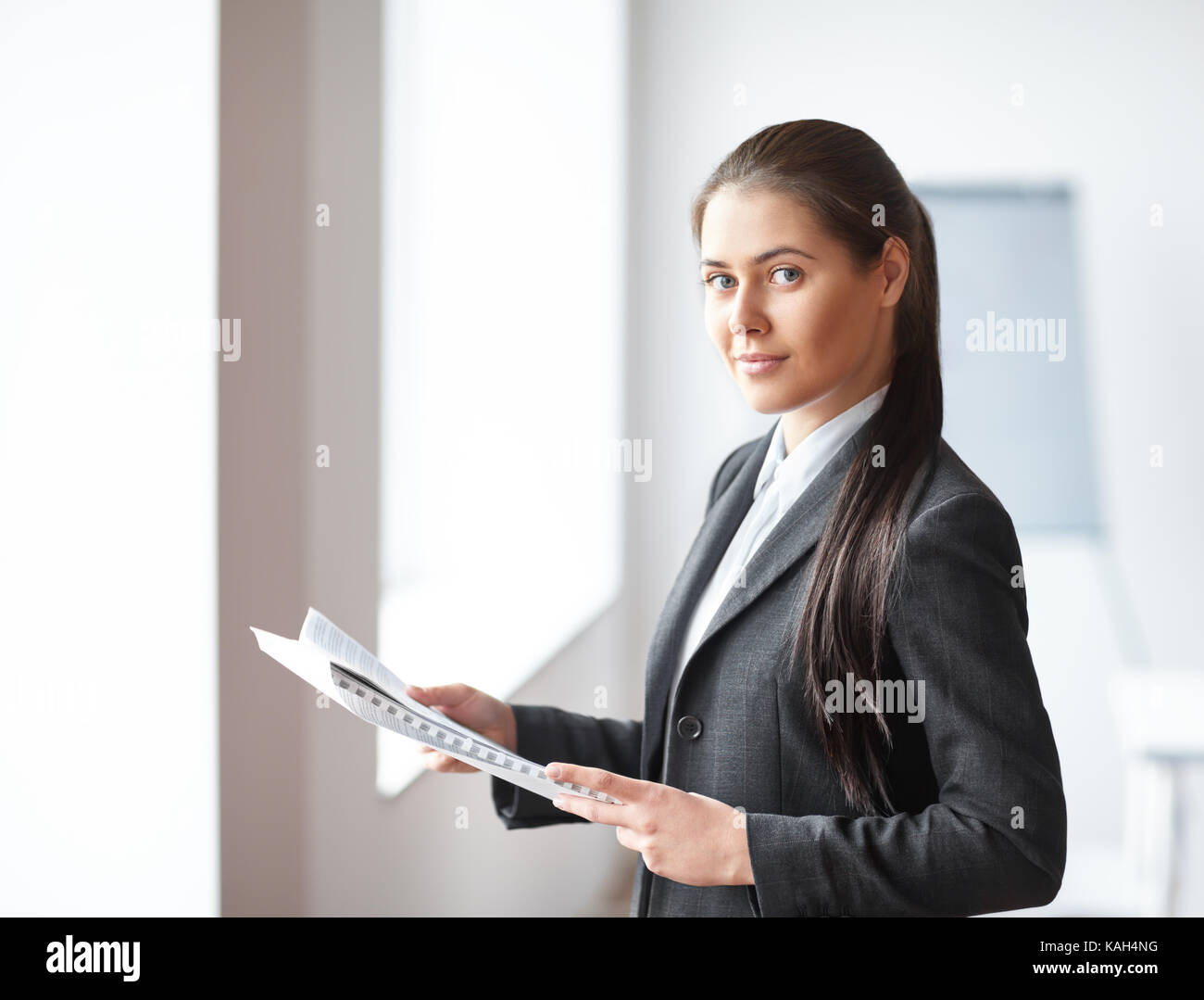 Portrait of young beautiful business woman with documents in the office ...