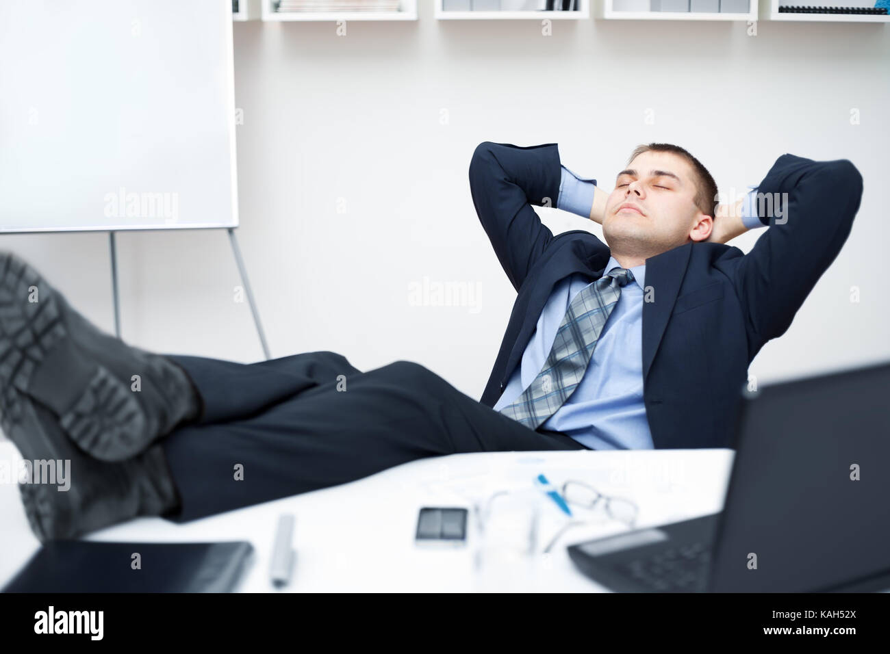 Tired businessman sleeping on chair in office with his legs on the ...