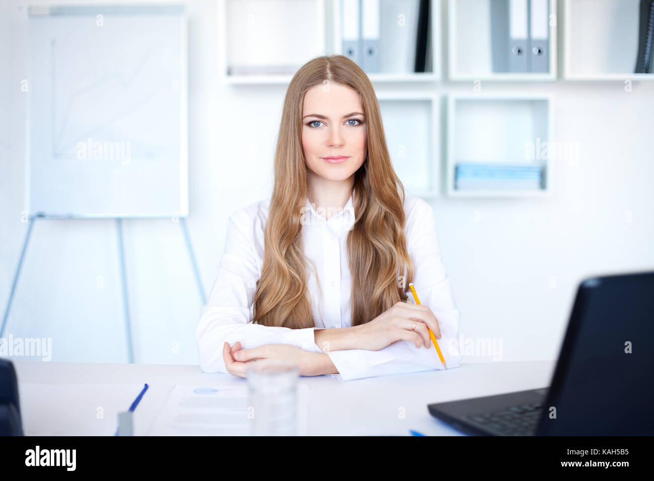 Portrait of beautiful young business woman sitting at desk in bright ...