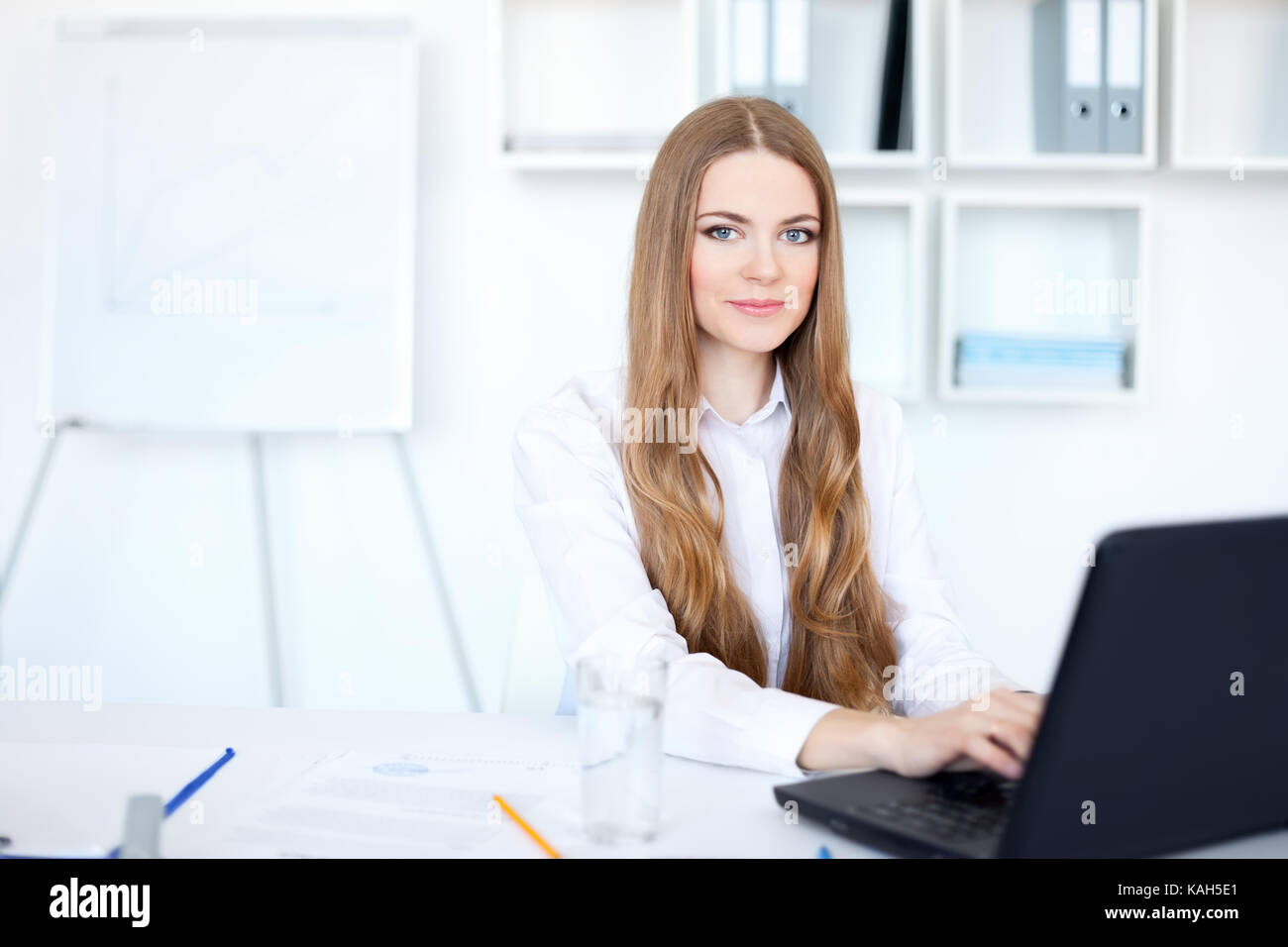 Portrait of beautiful young smiling business woman working on a laptop ...