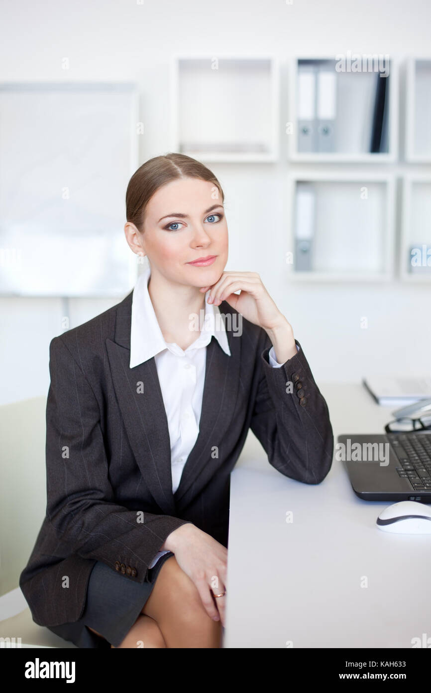 Portrait of beautiful young business woman sitting at desk at office ...