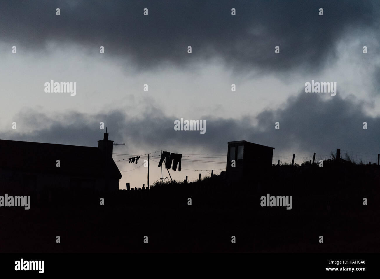 silhouette of simple rural house washing line and outbuilding in uk on a bleak windy evening Stock Photo