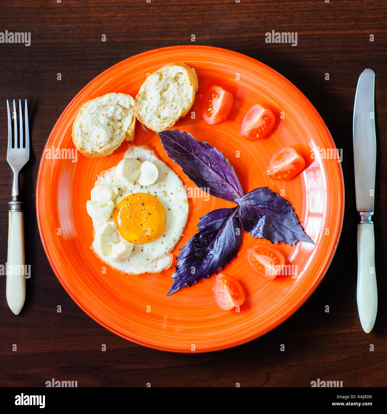 fried eggs mozzarella with basil and tomatoes on orange plate Stock