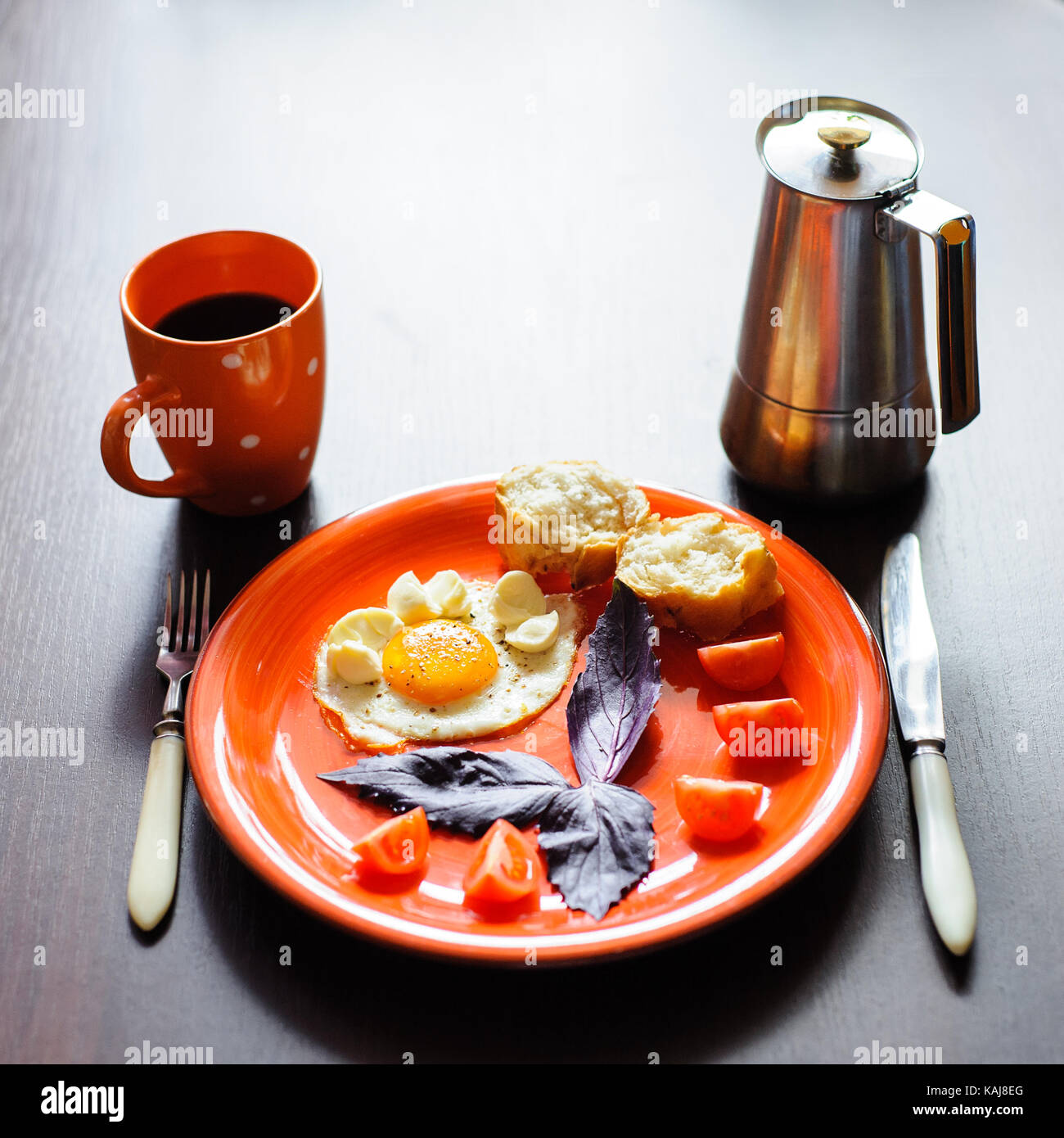 fried eggs mozzarella with basil and tomatoes on orange plate Stock