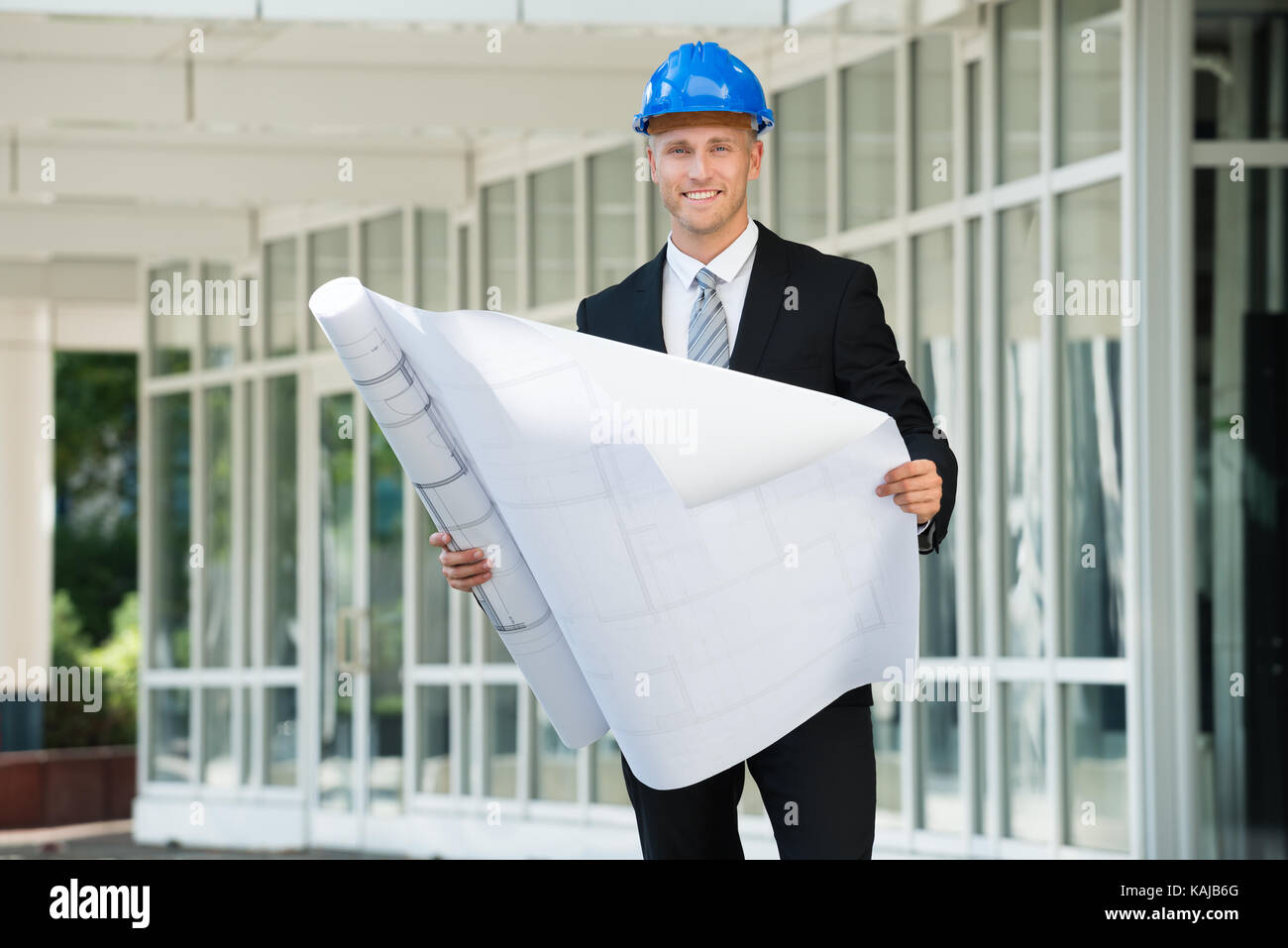 Young Engineer In Helmet Smiling While Examining Construction Project Stock Photo