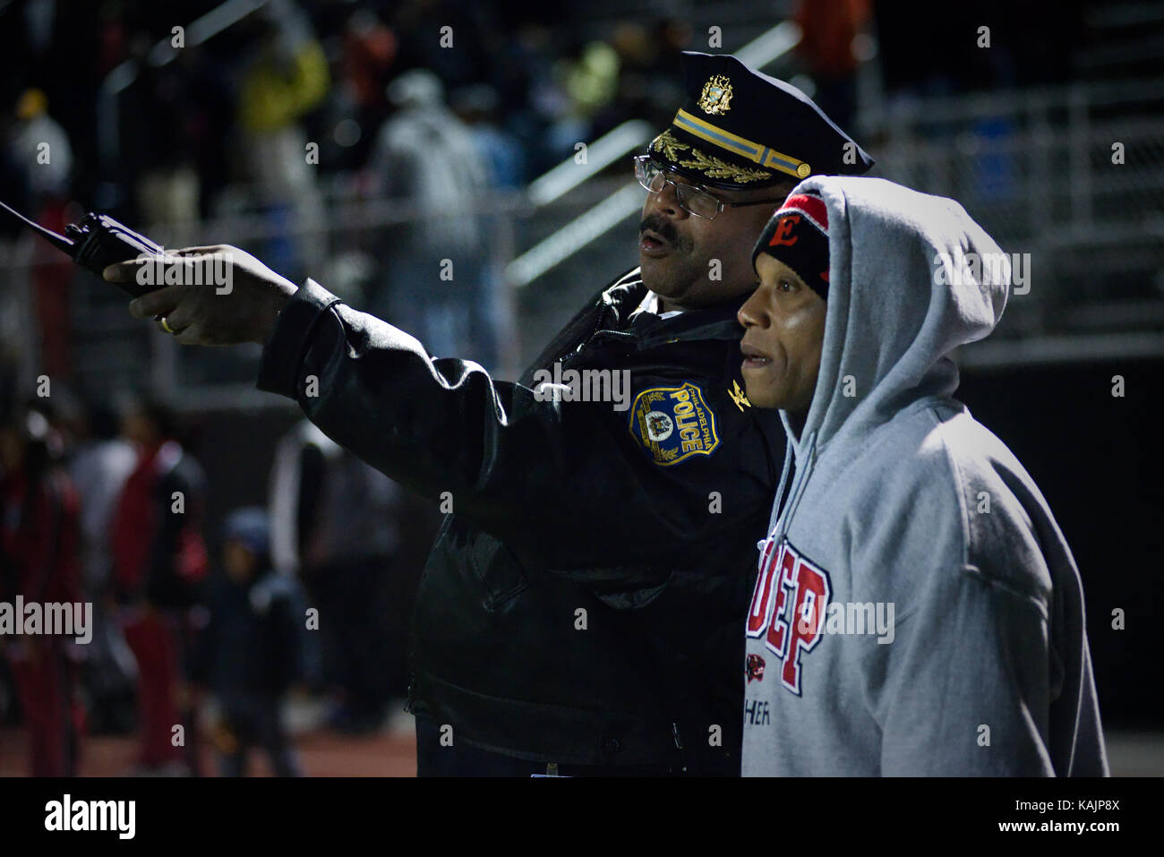Philadelphia, PA, USA - November 15, 2013; Police officer and coaching staff discuss game play from the side lines of a high school football game, in  Stock Photo