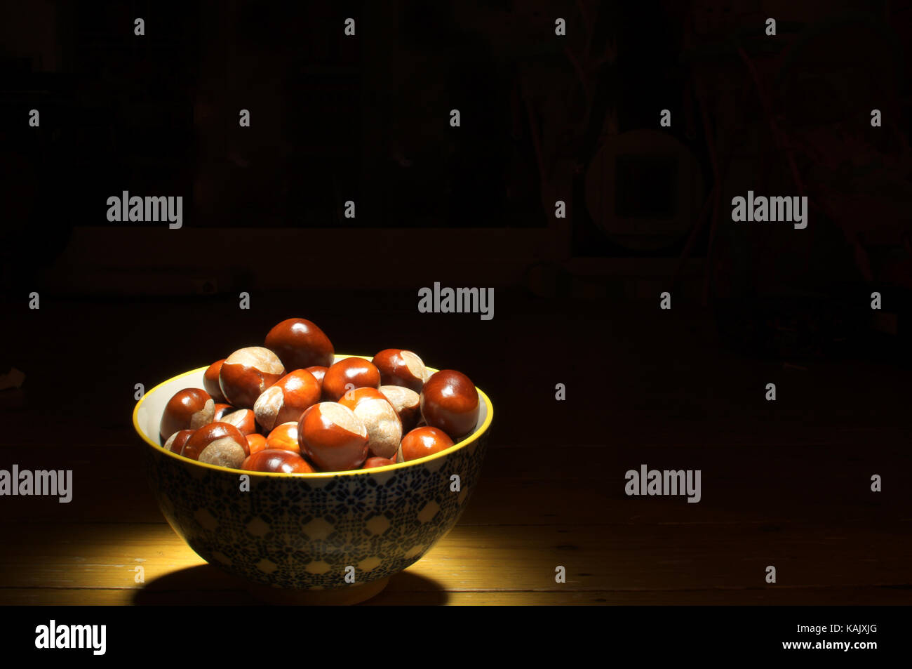 Bowl of conkers with a light shining on them against a black background Stock Photo