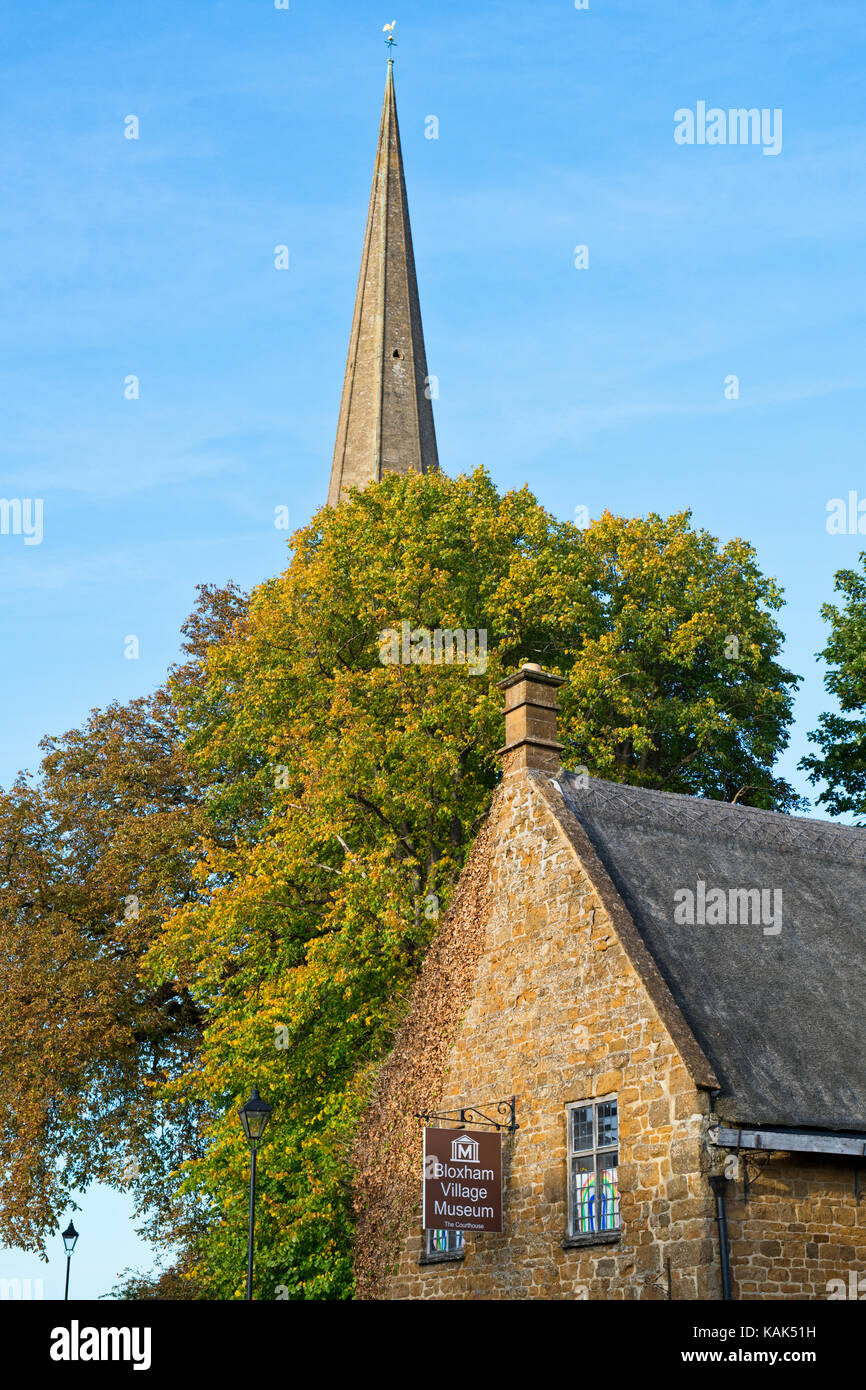 Bloxham village museum and autumn trees in front of the church spire against a bright blue sky in september. Bloxham, Oxfordshire , England Stock Photo