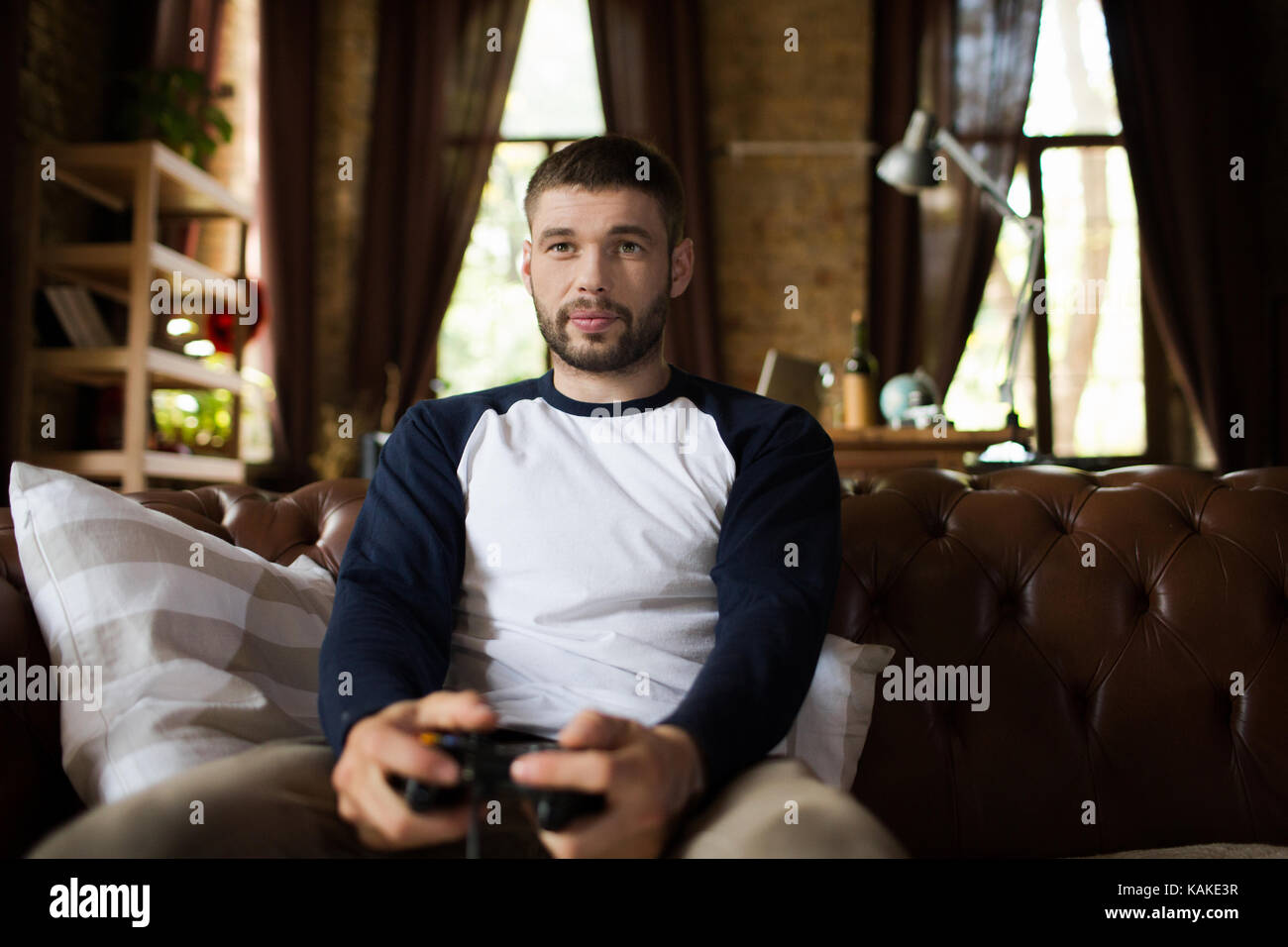 View of young man sitting on couch holding game controller joystick. Stock Photo
