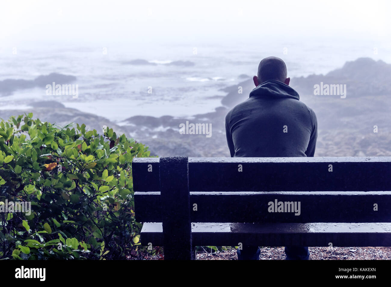 Sad and lonely man sitting on bench overlooking sea on Vancouver Island Stock Photo